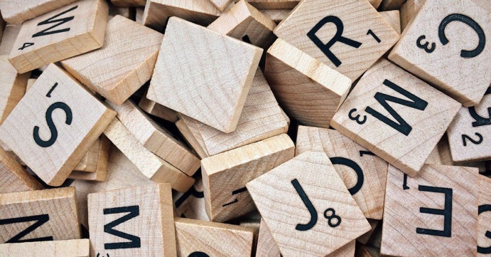 A collection of wooden Scrabble tiles with letters and numbers stacked randomly.