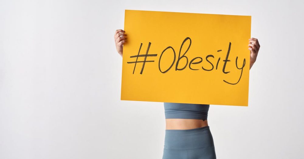 Individual holding yellow sign with hashtag 'Obesity'. Awareness concept.