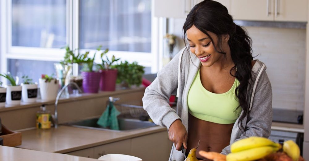 Smiling woman preparing fresh fruit in a sunlit kitchen, embodying a healthy lifestyle.