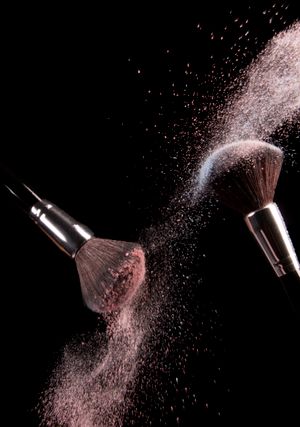 High-speed capture of makeup brushes dispersing pink powder in motion against a dark background.
