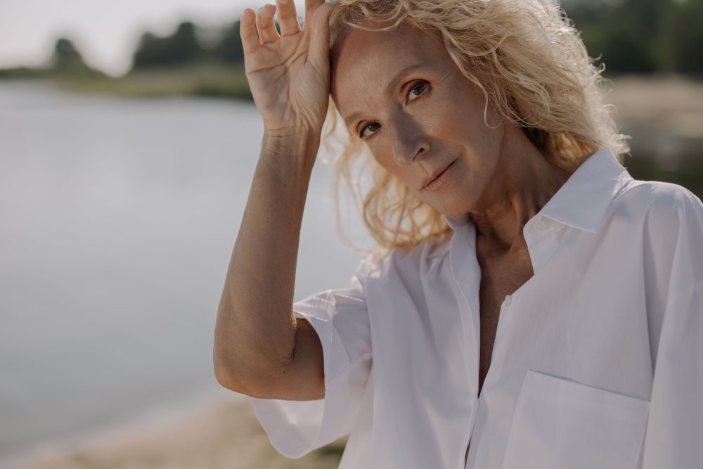 Portrait of a senior woman with blonde hair posing outdoors in sunlight.